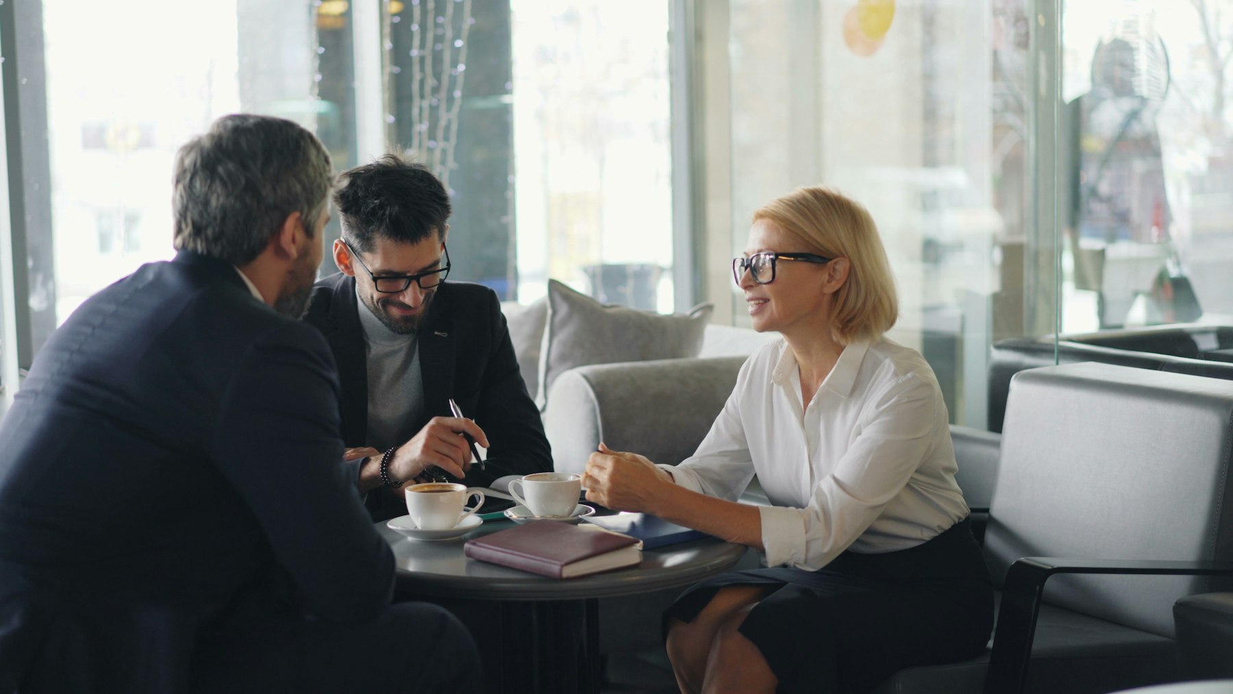 Zwei Männer und eine Frau im Gespräch an einem Tisch mit Unterlagen – Erben besprechen den Verkauf der geerbten Immobilie - Quelle: Unsplash (Lizenz: Unsplash License)