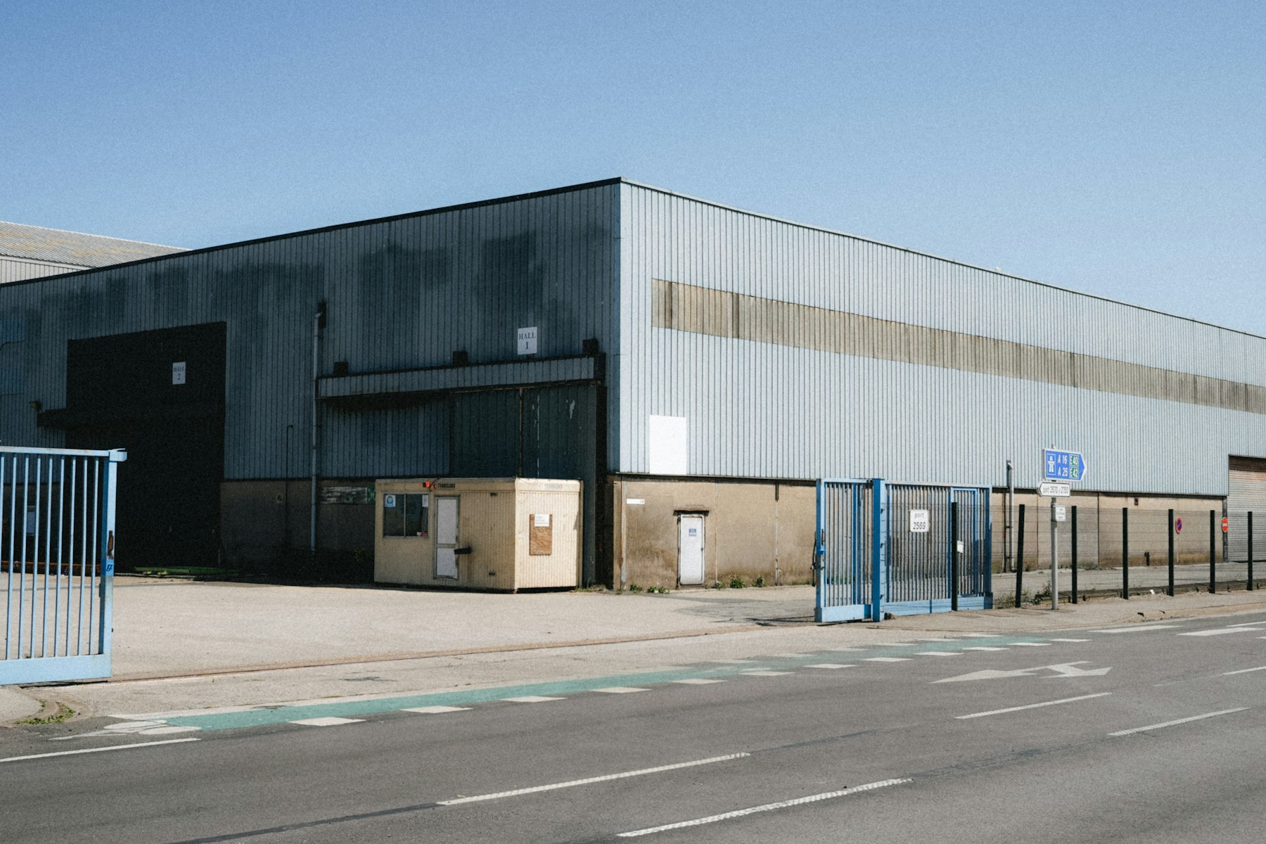 Große Gewerbehalle mit blauen Toren an einer Straße – Unternehmensimmobilie diskret verkaufen - Quelle: Unsplash (Lizenz: Unsplash License)