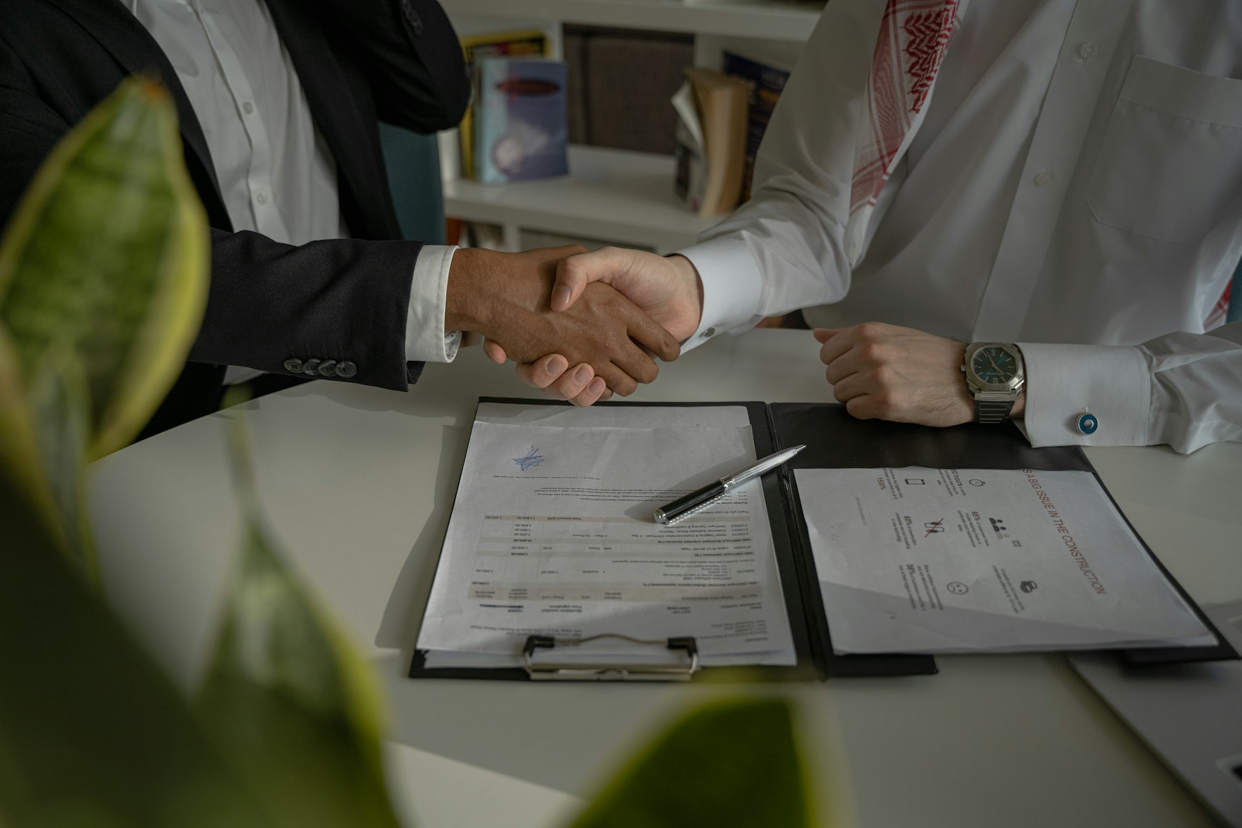 Zwei Geschäftsleute reichen sich über einem Tisch mit Vertragsunterlagen die Hand – Abschluss beim diskreten Immobilienverkauf - Quelle: Unsplash (Lizenz: Unsplash License)