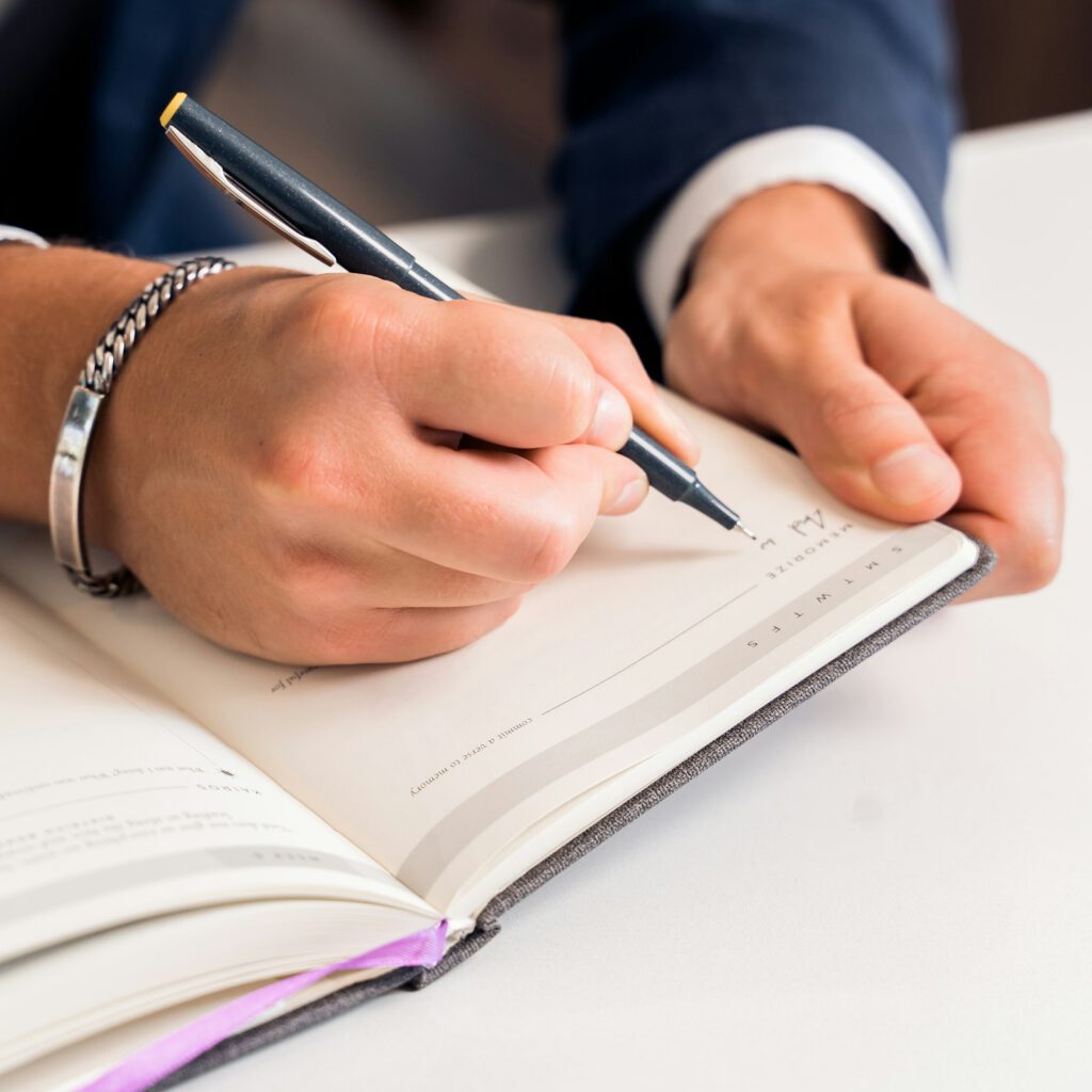 Hände im Anzug notieren im Notizbuch – Beratung zu Wertermittlung und Immobilienverkauf