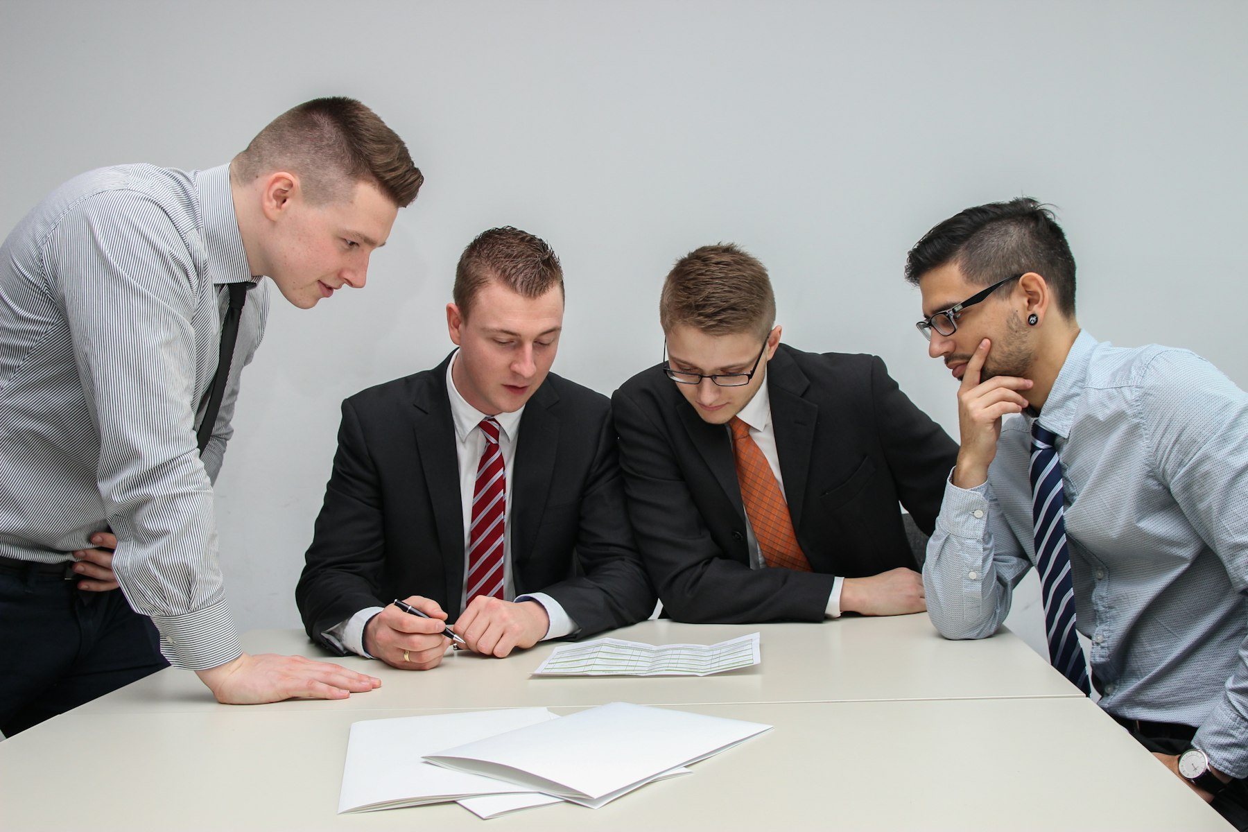 Vier Männer in Hemd und Krawatte prüfen gemeinsam Unterlagen an einem Besprechungstisch – Due Diligence beim Verkauf einer Büroimmobilie - Quelle: Unsplash (Lizenz: Unsplash License)