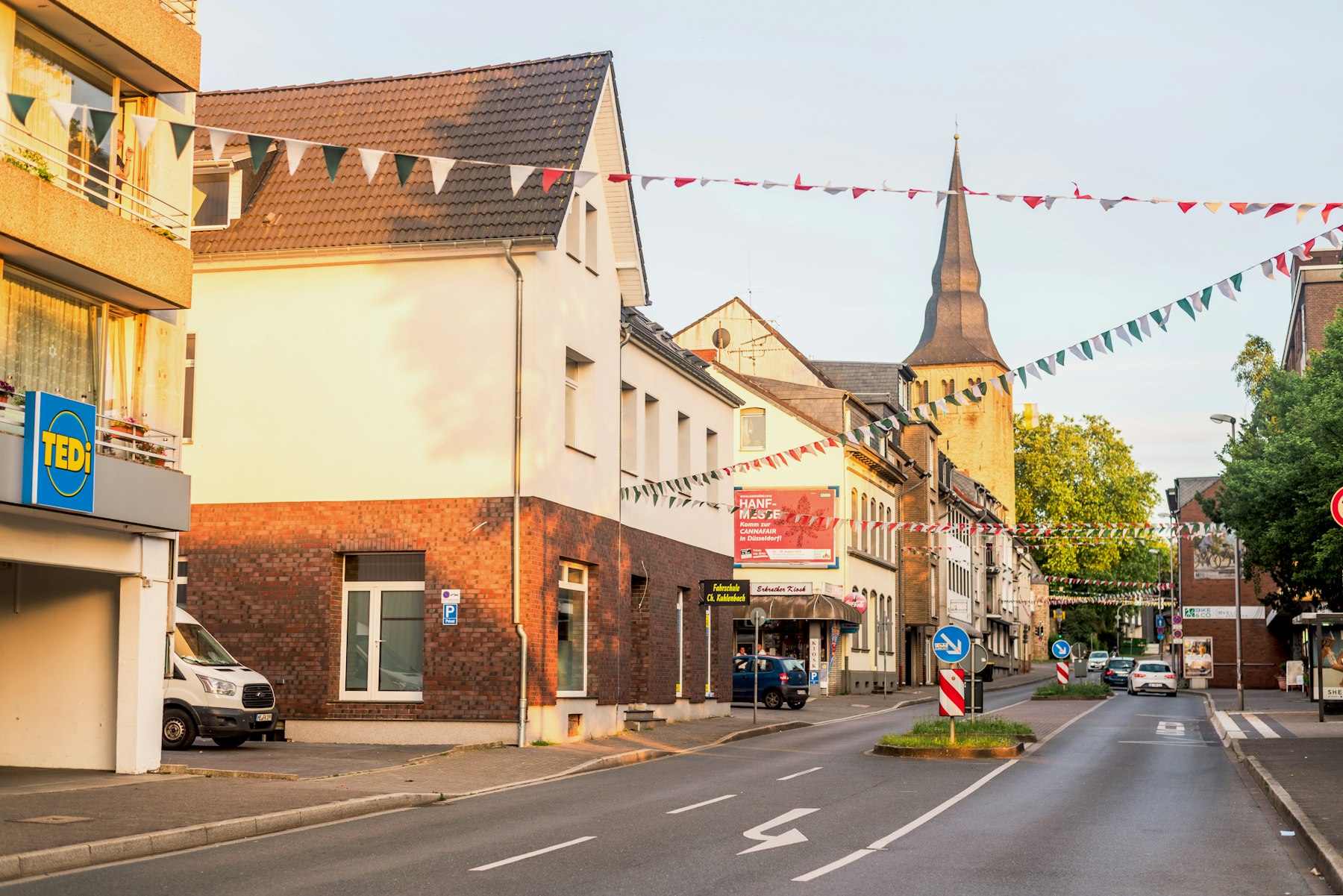 Innerstädtische Straße mit Wohn- und Geschäftshäusern, Läden im Erdgeschoss und einem Kirchturm im Hintergrund - Quelle: Unsplash (Lizenz: Unsplash License)