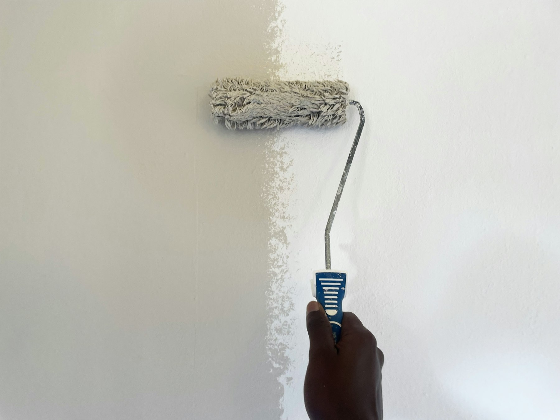 Hand mit Farbroller streicht eine Wand in hellem Weiß – Schönheitsreparaturen vor dem Hausverkauf - Quelle: Unsplash (Lizenz: Unsplash License)